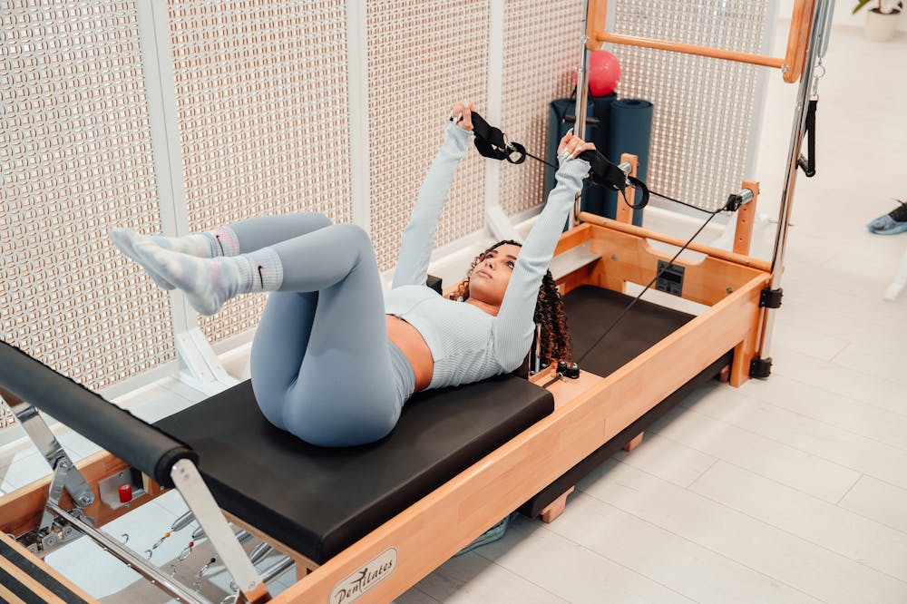 Mulher concentrada, usando calça cinza, enquanto faz pilates. Ilustração do texto sobre pilates para atletas.