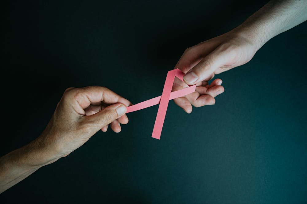 Mãos segurando fita cor de rosa. Ilustração do texto sobre outubro rosa.