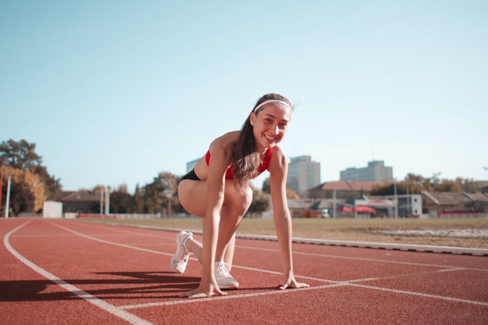 Mulher sorridente, em pista laranja, se preparando para a corrida. Ilustração do texto sobre benefícios do pilates para atletas.