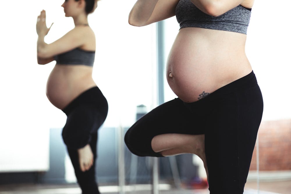 Gestante fazendo exercícios físicos enquanto usa calça legue na cor preta. Ilustração do texto sobre pilates para gestantes.