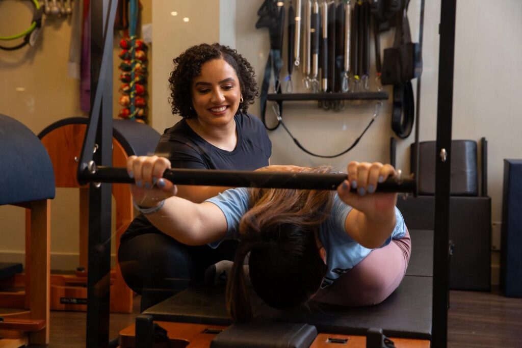 Fisioterapeuta sorridente, usando roupa preta, enquanto atende uma paciente. Ilustração do texto sobre benefícios do pilates para atletas.