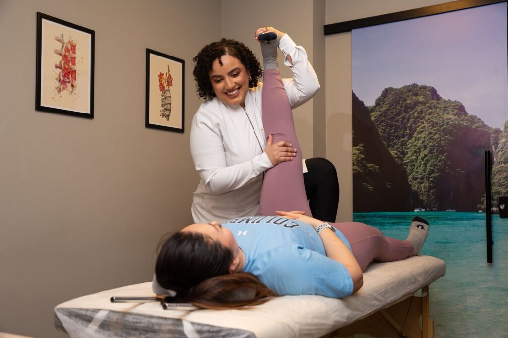 Fisioterapeuta sorridente, usando jaleco branco, enquanto atende uma paciente. Ilustração do texto sobre benefícios do pilates para atletas.